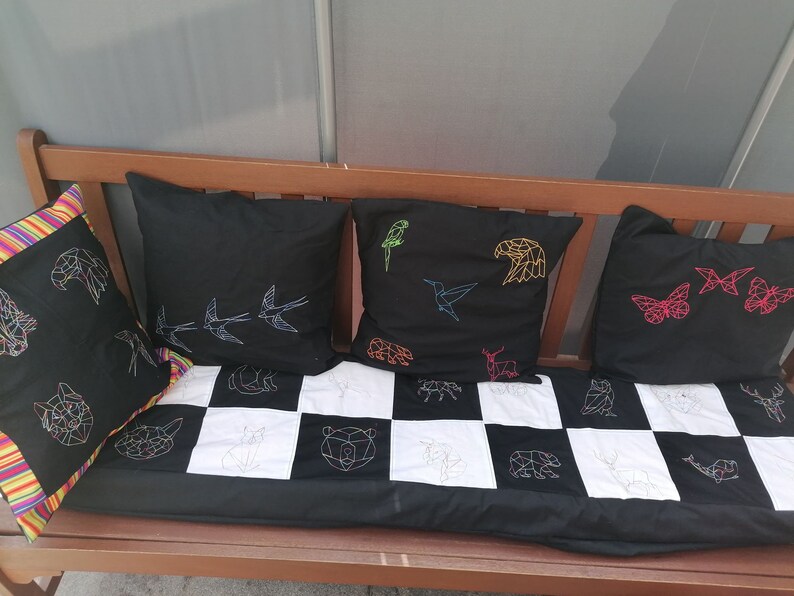 May include: A black bench with four black and white geometric patterned pillows. The pillows have colorful embroidery of animals and birds, including a butterfly, a hummingbird, a bird, and an eagle.