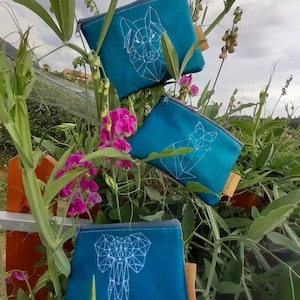 May include: Three teal blue zippered pouches with white geometric animal designs. The pouches feature a wolf, a fox, and an elephant.