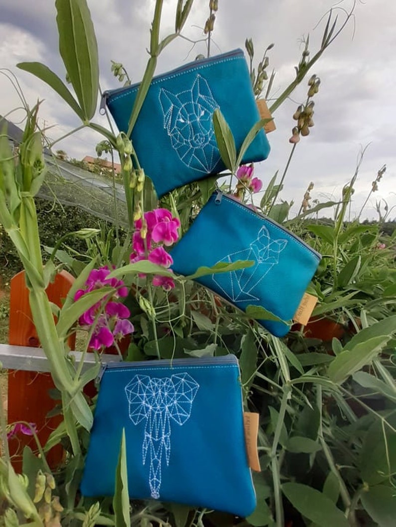 May include: Three teal blue zippered pouches with white geometric animal designs. The pouches feature a wolf, a fox, and an elephant.