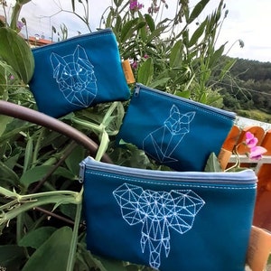 May include: Three teal zippered pouches with white geometric animal designs. The pouches feature a wolf, a fox, and an elephant.