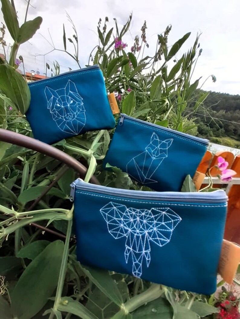 May include: Three teal zippered pouches with white geometric animal designs. The pouches feature a wolf, a fox, and an elephant.