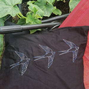 May include: Black pillow with three white embroidered swallows. The pillow is on a red chair.