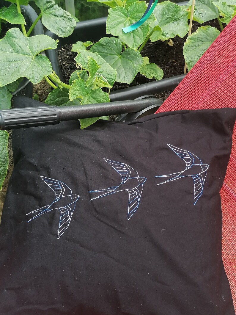 May include: Black pillow with three white embroidered swallows. The pillow is on a red chair.