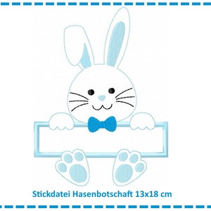 Puede incluir: Un conejo azul y blanco con una pajarita azul sostiene un cartel azul en blanco. El cartel mide 13x18 cm. El texto "Stickdatei Hasenbotschaft 13x18 cm" está debajo del conejo.