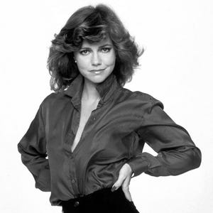 May include: A black and white photograph of a person wearing a dark red button-down shirt and black pants. The person is posing with one hand on their hip. The shirt is unbuttoned at the top. The image has a watermark that says "DO NOT COPY".