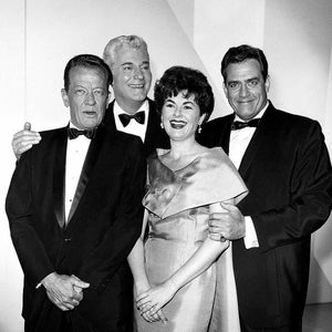 May include: A black and white photo of four people in formal attire. Two men are wearing black suits and bow ties, while a woman is wearing a dress and a man is wearing a suit and bow tie. The woman is standing between the two men in suits.