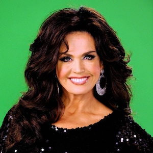 May include: A woman with long dark brown hair wearing a black sequined dress and large diamond earrings. She is smiling and looking at the camera.