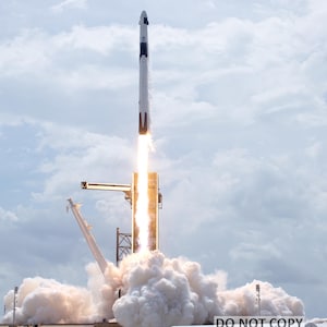 May include: A white and black rocket launches from a launchpad, leaving a trail of smoke and fire.