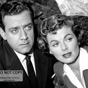 May include: A black and white photo of a man and a woman. The man is wearing a suit and tie, and the woman is wearing a jacket and blouse. The man has his arm around the woman's shoulder. The photo is likely from a television show or movie.