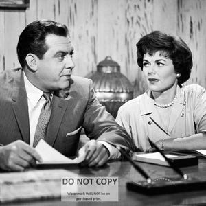 May include: A black and white photo of a man and a woman sitting at a table. The man is wearing a suit and tie, and the woman is wearing a dress. They are both looking at the camera.