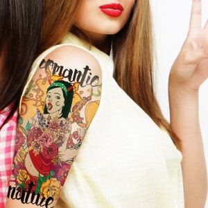 Op de afbeelding: Een tijdelijke tattoo met een kleurrijke illustratie van een vrouw met een duivelshoorn-hoofdband, omringd door bloemen en de woorden "romantic nature".