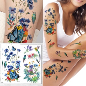 May include: Two temporary tattoo sheets with a floral design featuring blue flowers, green leaves, butterflies, and hummingbirds. The tattoos are on a white background.