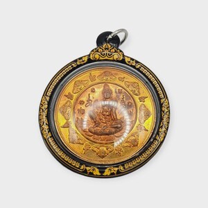 Könnte beinhalten: Ein runder, goldfarbener Anhänger mit einem detaillierten Relief einer sitzenden Figur, möglicherweise einer Gottheit, in einem transparenten Rahmen. Der Anhänger hat einen schwarz-goldenen Zierrand und einen silberfarbenen Ring oben.