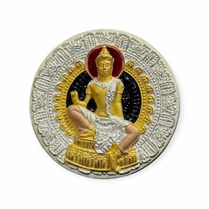 Könnte beinhalten: Ein runder, silberfarbener Anhänger mit einer goldfarbenen Buddha-Figur in der Mitte. Der Buddha sitzt mit gekreuzten Beinen und Händen in meditativer Haltung. Der Anhänger ist von einem dekorativen Rand umgeben.