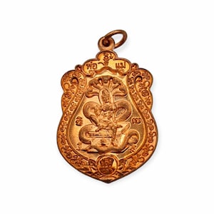 Könnte beinhalten: Ein goldfarbener Anhänger mit einer detaillierten Darstellung einer mehrköpfigen Schlange, bekannt als Naga, die sich um eine Schatztruhe windet. Der Anhänger hat oben eine Schlaufe zum Anbringen an einer Kette. Die Inschrift "พ่อ แม่" ist auf dem Anhänger sichtbar.