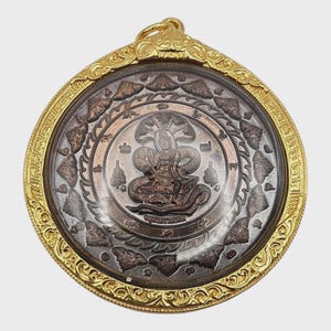 Könnte beinhalten: Runder, goldfarbener Anhänger mit detailliertem Design. Die Mitte zeigt eine sitzende Figur mit einer mehrköpfigen Schlange, umgeben von komplizierten Mustern. Der Anhänger hat einen goldfarbenen Rahmen und eine Schlaufe zum Aufhängen.