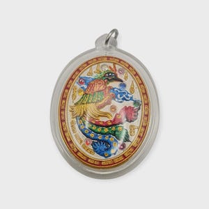 May include: Oval pendant featuring a colorful phoenix design. The phoenix has red, green, yellow, and blue feathers, set against a textured background. The pendant is encased in a clear plastic with a metal loop at the top.