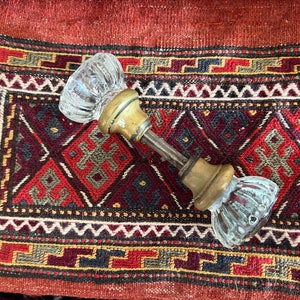 May include: A vintage glass door knob with a brass base and a ribbed design. The knob is set against a colorful, patterned rug with red, black, and gold tones. A classic hardware piece.