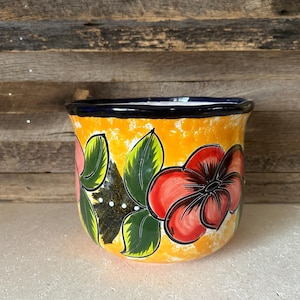 Könnte beinhalten: Ein handbemalter Keramiktopf mit einem lebendigen Blumendesign. Der Topf hat einen leuchtend gelben Hintergrund mit großen roten und rosa Blumen, grünen Blättern und einem dunkelblauen Rand. Dieser dekorative Topf ist ideal für Zimmerpflanzen.