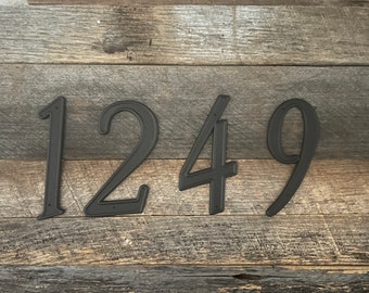 May include: Four black metal house numbers: 1, 2, 4, and 9, are displayed against a weathered wood background. The numbers have a textured surface and a classic font, suitable for outdoor use. The numbers are approximately 6 inches tall.