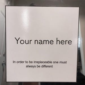 May include: A white sign with black text that reads "Your name here" and "In order to be irreplaceable one must always be different". The sign has a black border.