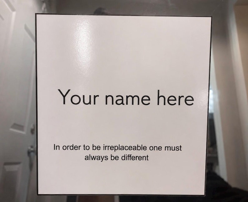 May include: A white sign with black text that reads "Your name here" and "In order to be irreplaceable one must always be different". The sign has a black border.
