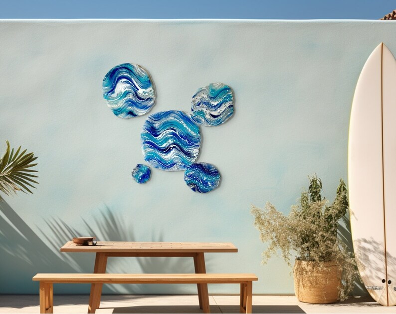 May include: Abstract wall art in blue and white, mimicking waves, adorns a light blue wall. A wooden table and bench are positioned below, with a surfboard nearby. The artwork and setting create a coastal atmosphere, reminiscent of a seaside location.