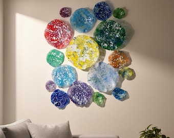May include: A wall art installation featuring a collection of colorful, circular glass pieces. The pieces vary in size and color, including red, blue, yellow, and green, creating a vibrant and artistic display. The installation is mounted on a neutral-toned wall.