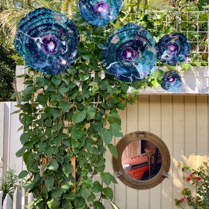 May include: A collection of four circular, multi-coloured glass wall art pieces featuring swirling patterns of deep blue, purple, and teal with white accents, mounted on a white wire trellis above a round, brass-rimmed porthole-style mirror.