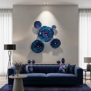 May include: A set of five circular wall art pieces in varying sizes, featuring a deep blue and purple swirling pattern with a glossy finish. The pieces are arranged in a cluster on a wall above a blue sofa, creating a focal point with their concentric, textured appearance and vibrant, reflective colour palette.