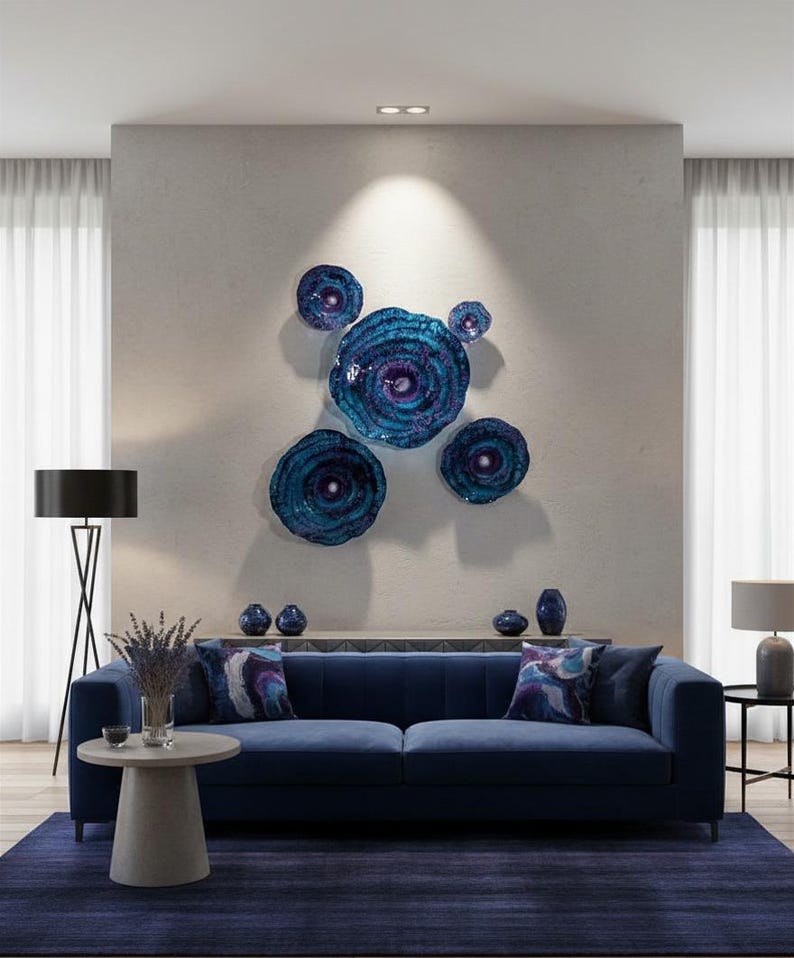 May include: A set of five circular wall art pieces in varying sizes, featuring a deep blue and purple swirling pattern with a glossy finish. The pieces are arranged in a cluster on a wall above a blue sofa, creating a focal point with their concentric, textured appearance and vibrant, reflective colour palette.