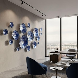 May include: A collection of circular wall art pieces in varying sizes, featuring a textured, mottled blue and white finish. These round, disc-like objects are arranged in a cluster on a light gray wall, creating a dimensional display.