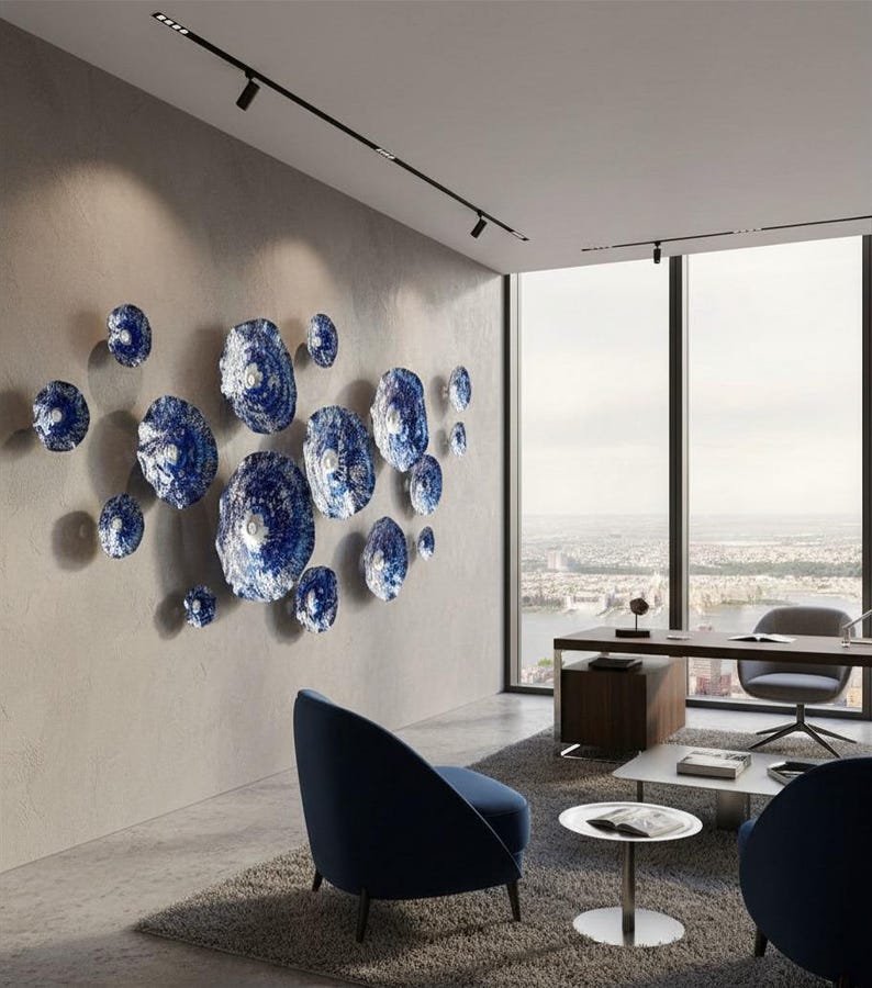 May include: A collection of circular wall art pieces in varying sizes, featuring a textured, mottled blue and white finish. These round, disc-like objects are arranged in a cluster on a light gray wall, creating a dimensional display.