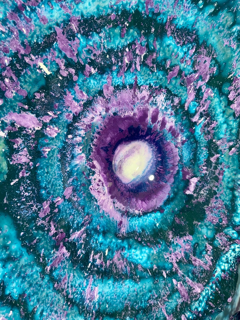 May include: An abstract painting featuring a circular, vortex-like composition with concentric rings of vibrant turquoise, deep teal, and various shades of purple. The centre contains a bright white and light lavender core with textured paint.