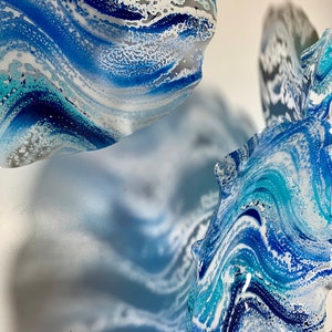 May include: Abstract artwork with swirling patterns in shades of blue, white, and grey. The design evokes flowing water or marble, with a textured, layered look. The piece has a contemporary, artistic style.