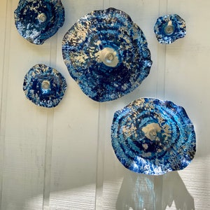 May include: A set of five circular wall art pieces featuring a deep blue and silver mottled finish with wavy, irregular edges. The pieces vary in size, with a large central disc, two medium discs, and two smaller discs, all displaying a textured, metallic appearance.