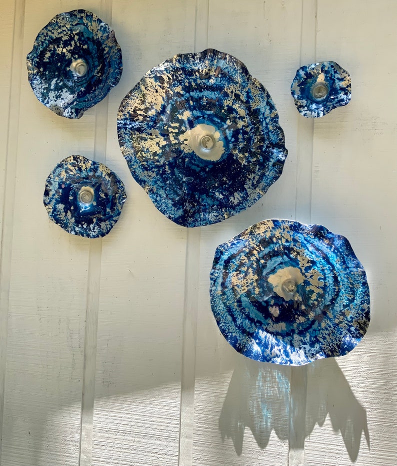 May include: A set of five circular wall art pieces featuring a deep blue and silver mottled finish with wavy, irregular edges. The pieces vary in size, with a large central disc, two medium discs, and two smaller discs, all displaying a textured, metallic appearance.