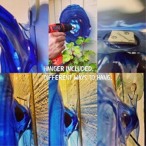 May include: A series of images demonstrating how to hang a blue, abstract art piece. The images show a hook, a drill, and a Velcro strip being used. The text "HANGER INCLUDED. DIFFERENT WAYS TO HANG." is displayed.