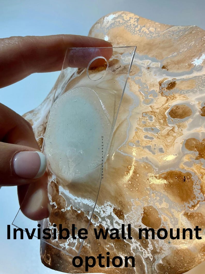May include: A transparent, rectangular wall mount option is held against a textured, abstract art piece with brown, white, and gold tones. The text "Invisible wall mount option" is printed at the bottom of the image.