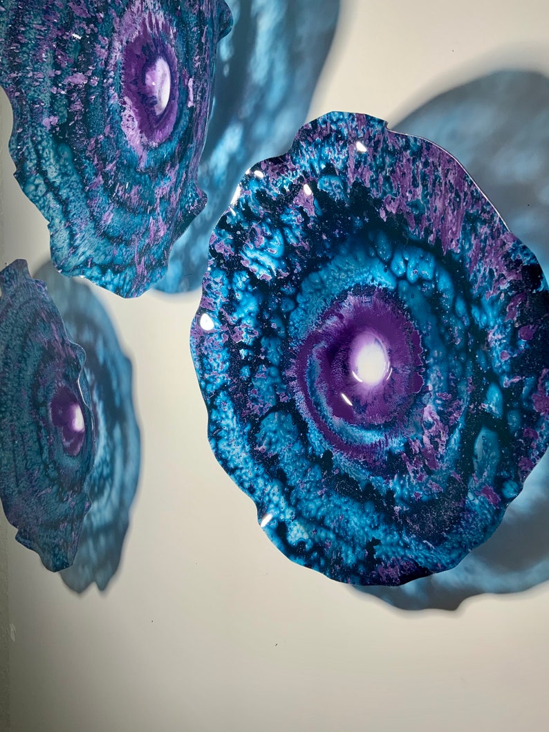 May include: Three circular wall art pieces featuring a swirling abstract pattern in shades of deep purple, royal blue, and teal. Each piece has a glossy, reflective finish with a central white core, creating a galaxy-like appearance with organic, wavy edges.