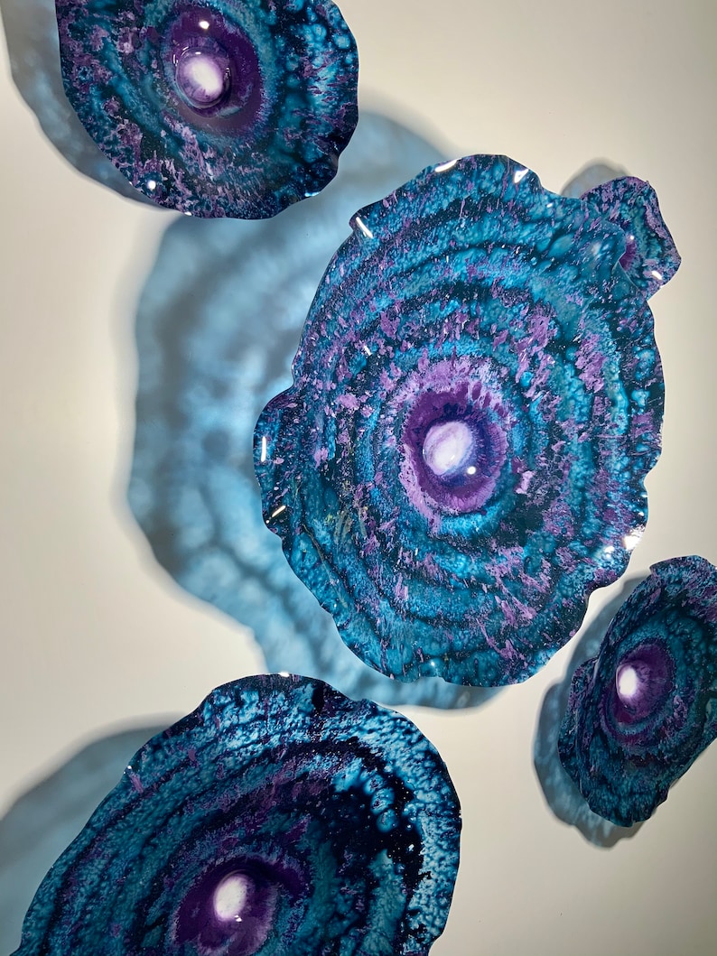 May include: Four circular resin coasters featuring a swirling pattern of deep blue, teal, and purple hues. Each piece has a prominent white centre surrounded by concentric rings of colour, creating a textured, agate-like appearance with a glossy finish.