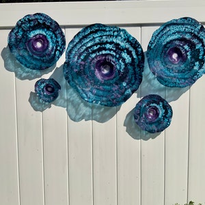May include: A set of five circular wall art pieces featuring a textured, swirling pattern in shades of deep blue, teal, and purple. Each piece has a concave centre and a translucent, glass-like appearance with organic, irregular edges.