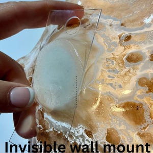 May include: A clear acrylic wall mount attachment with a circular hole at the top, positioned against a decorative bowl featuring a marbled pattern of white and metallic gold swirls. The text Invisible wall mount option is visible.