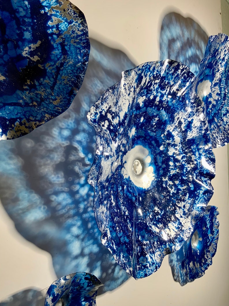 May include: A wall art installation consisting of multiple circular, bowl-shaped discs with wavy, irregular edges. The discs feature a vibrant blue and white mottled pattern with a glossy, reflective finish, creating a textured appearance.
