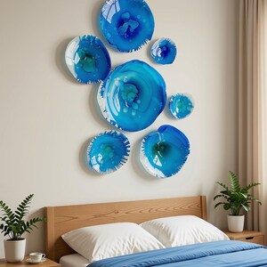 May include: A collection of seven circular wall art pieces in varying sizes, featuring swirling patterns of deep blue, bright azure, and white. The glossy, translucent discs are arranged in a cluster, creating a vibrant focal point on the wall.