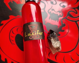 Pode incluir: Uma garrafa de vidro vermelha com um rótulo preto que diz "Lucifer" em letras amarelas. A garrafa tem um bico de pulverização preto e está sobre uma superfície vermelha e preta.