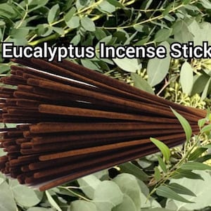 May include: A bundle of brown eucalyptus incense sticks, arranged in a fan shape, with green eucalyptus leaves in the background. The text "Eucalyptus Incense Sticks" is displayed above the sticks.