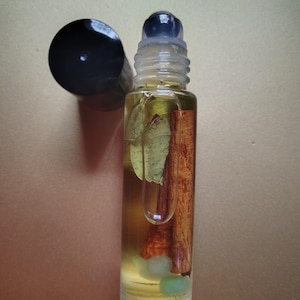 May include: A clear glass roller bottle with a black cap and a black roller ball. The bottle is filled with a light yellow liquid and contains small green and brown pieces.