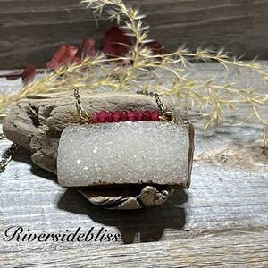 May include: A white agate pendant necklace with a gold chain and a row of pink beads. The pendant is a rectangular shape with a rough, textured surface.