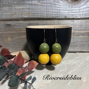 May include: A pair of dangle earrings with two round beads on each earring. The top bead is green with a textured surface and the bottom bead is yellow.